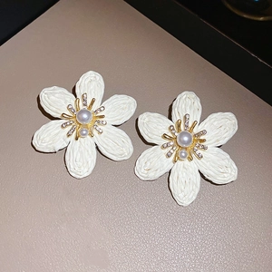 Detail of woven white flower earrings featuring pearl center and rhinestone accents