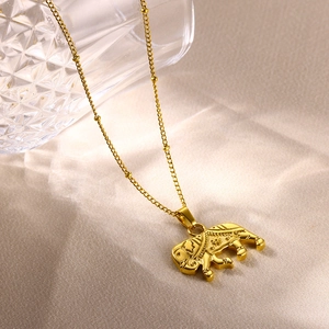 Macro shot of a polished golden elephant pendant on a beaded chain over beige silk fabric