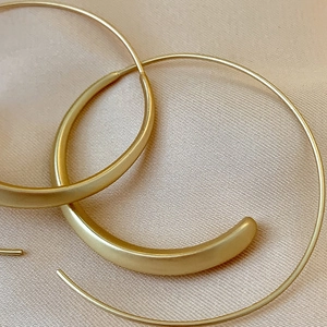 Detailed close-up of gold matte geometric C-shaped hoop earrings on beige silk fabric