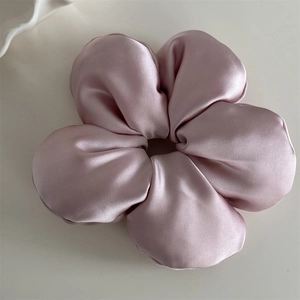 Close-up of pink silk flower scrunchie with soft satin texture on a beige background