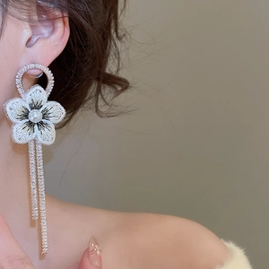 Détail de boucle d'oreille fleur en maille blanche avec perle et pompons en strass