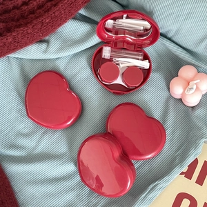 Deep red heart-shaped contact lens case set with mirror and tools on soft fabrics
