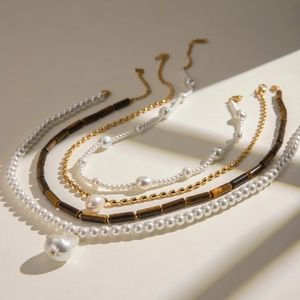 Layered stainless steel necklace with baroque pearls and tiger eye beads on white surface
