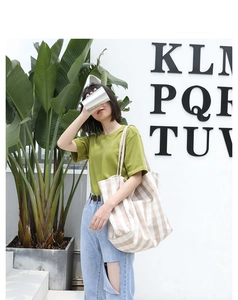Detail of a large beige striped canvas tote bag held by a model in casual attire