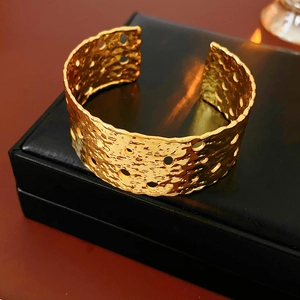 Macro detail of wide gold cuff bracelet featuring hammered texture and hollow cut-outs