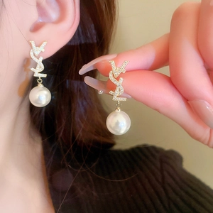 Détail de boucles d'oreilles dorées élégantes avec perles blanches et logo en cristal