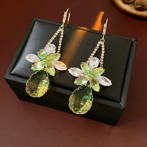 Macro shot of luxury gold earrings with green teardrop crystal and floral zircon studs