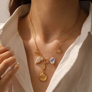 Detail of gold necklace featuring starfish, shell, pearl and bee charms on model