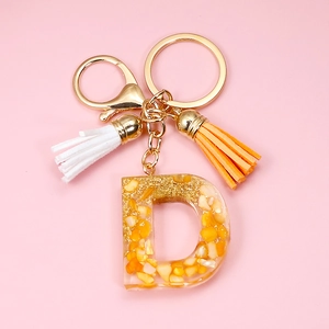 Detail of Letter D resin keychain with orange stones and decorative tassels on pink background