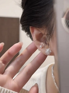 Detailed close-up of asymmetrical pearl and starburst stud earrings worn on the ear lobe