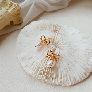 Gros plan de boucles d'oreilles nœuds dorés avec perles blanches sur socle texturé