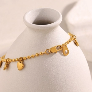 Elegant 18K gold-plated stainless steel bead bracelet with heart charms on a ceramic vase
