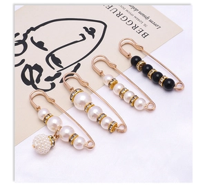 Macro detail of gold-plated safety pins with white pearls and black beads for waist adjustment