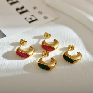 Macro view of C-shaped gold-plated stainless steel earrings with green and pink enamel