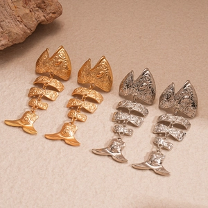 Exaggerated metal fishbone earrings in gold and silver finish on a textured background