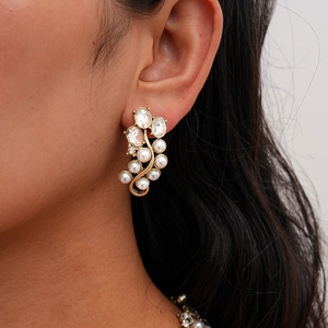 Close-up of gold-tone earrings featuring white imitation pearls and sparkling crystals