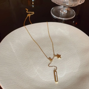 Detail of gold star and rectangular pearl pendant on a stainless steel Y-necklace