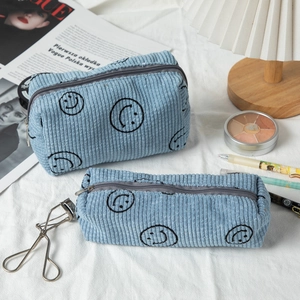 Blue corduroy makeup bags with black smiley face prints on a decorative lifestyle desk