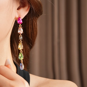 Detail of model wearing long teardrop earrings with colorful crystals and gold finish