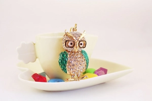 Vue macro porte-clés hibou en émail vert et cristaux sur un plat en céramique