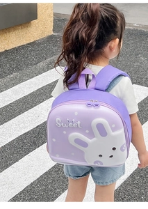Outdoor shot of a little girl wearing the purple cartoon rabbit eggshell backpack on a street