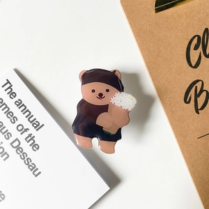 Detail shot of a cute brown bear acrylic phone grip holder with white flowers on white desk