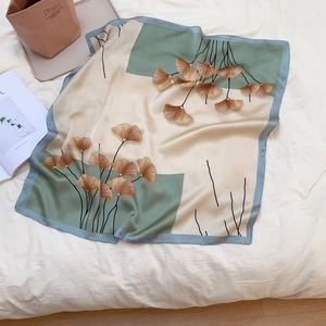 Detail of silk square scarf featuring golden ginkgo leaf patterns on beige and green fabric