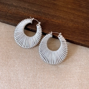 Minimalist silver woven hoop earrings with textured design on a rustic wooden background
