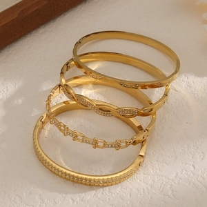 Set of four 18k gold plated stainless steel bangles with zircon crystals on stone background