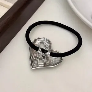 Retro black elastic hair tie with silver textured hollow heart metal charm on a white fabric