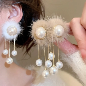 Close-up of elegant plush fur ball and pearl tassel earrings in white and khaki