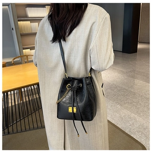 Vista modella di una borsa a secchiello nera con coulisse, catena dorata e tracolla