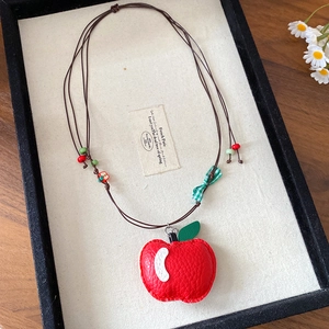Detail of red leather apple pendant with checkered bow on a brown cord necklace