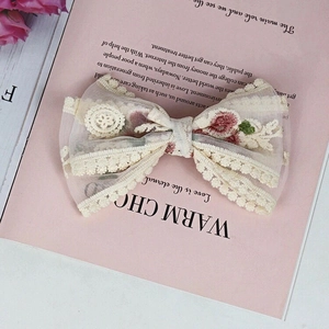 Detailed embroidery of pink flowers on beige lace bow hair clip with mesh texture