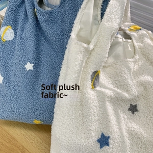 Close-up of starry planet embroidery on soft fleece texture of the blue and beige tote bag