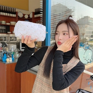 Close-up of white quilted makeup bag with cherry pattern held by a model in a cafe
