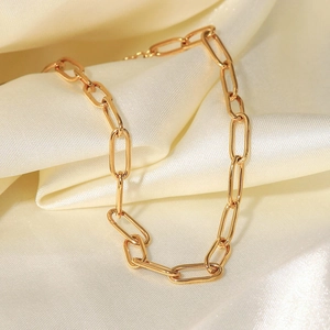 Detail of 18K gold paperclip link chain jewelry placed on a luxury silk fabric background