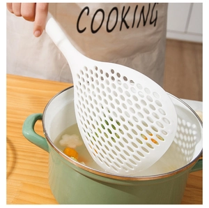 Action shot of large white slotted spoon draining food from a pot in a kitchen
