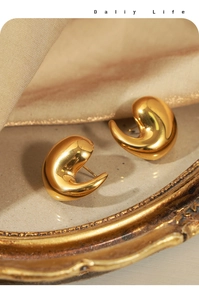 Macro detail of gold plated curved teardrop earrings on elegant silk fabric background