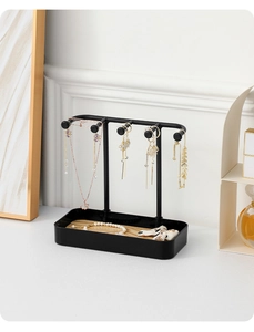 Detail of black metal jewelry organizer stand with hooks and light wood base tray