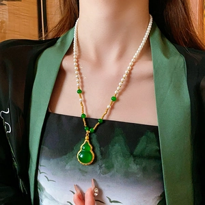 Détail d'un collier doré avec pendentif gourde, perles et petites billes vertes