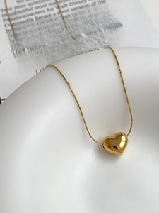 Detail of a polished gold heart pendant necklace on a ceramic tray over a magazine