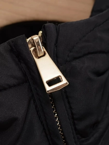 Detailed macro view of a high-quality gold metal zipper on a black quilted jacket