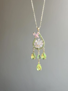 Macro detail of a gold necklace pendant featuring a pink butterfly and green teardrop gems