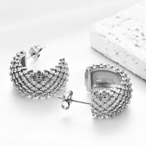 Detail macro view of silver C-shaped earrings with textured mesh grid pattern