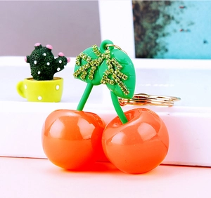 Detail of cherry keychain with orange-red resin fruit and sparkling green rhinestone leaves