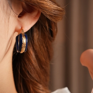 Dettaglio dell'orecchino a cerchio in smalto blu e oro indossato dalla modella