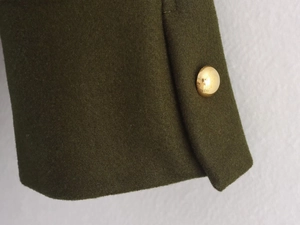 Close-up of dark green wool coat cuff with premium gold dome button detail