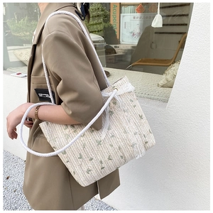 Detail of handwoven straw tote featuring green leaf embroidery and white lace trim edge