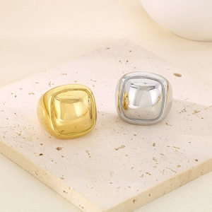 Detailed view of square chunky stainless steel rings in gold and silver on a stone pedestal